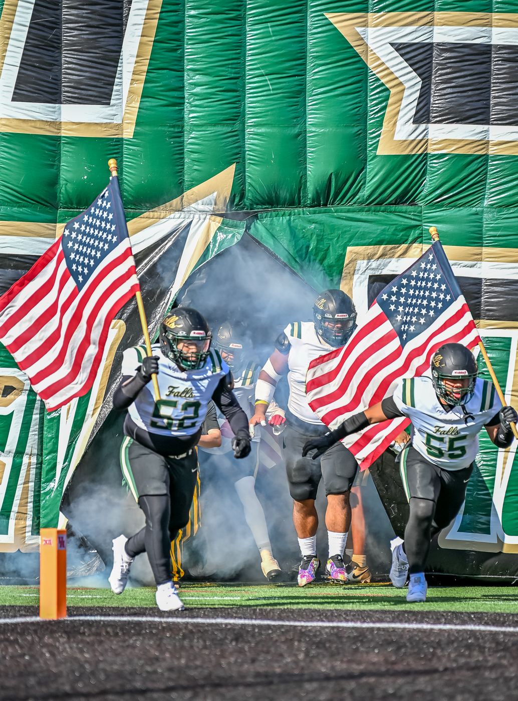 High school football players running onto the field carrying American flags before a game, shot by a real working sports photographer