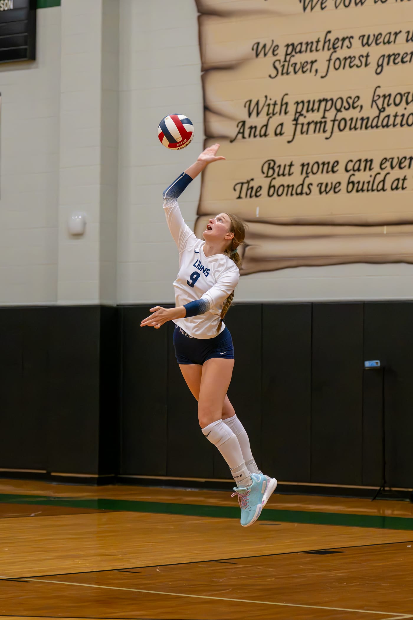 A high school volleyball player mid-serve, shot by a real working sports photographer