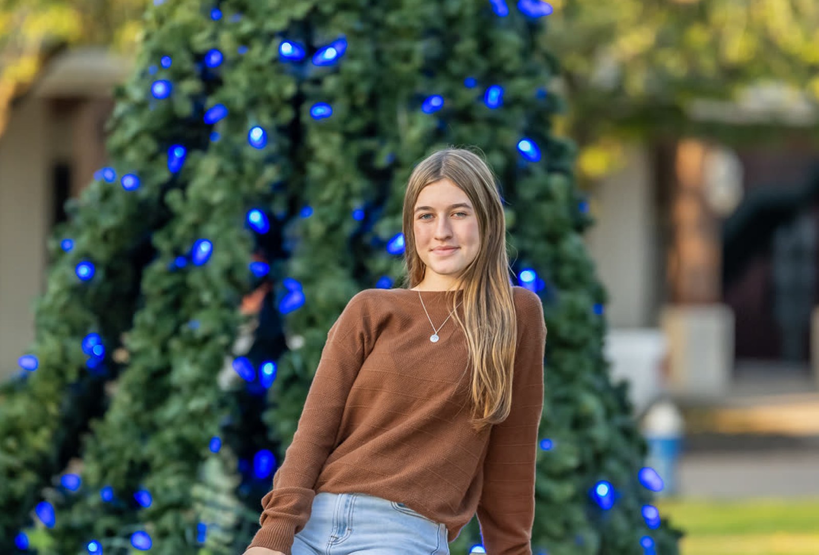 A teenage girl posing for a holiday mini-session portrait beside a lit Christmas tree, shot by a real working photographer